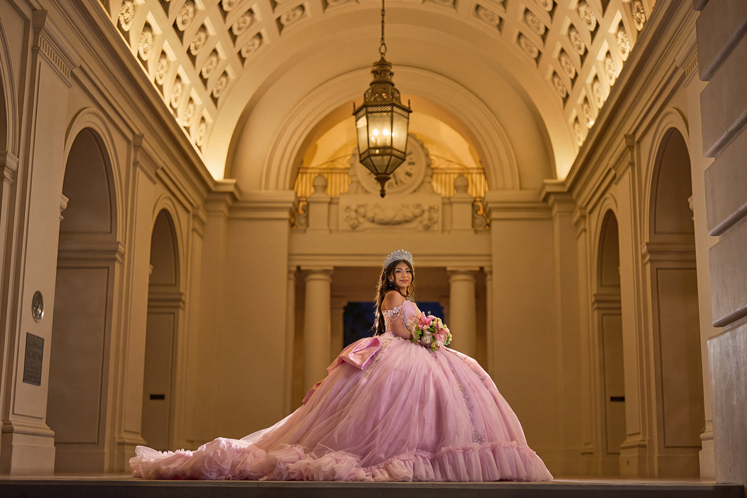 Quinceañera in pink ballgown beneath a golden vaulted archway