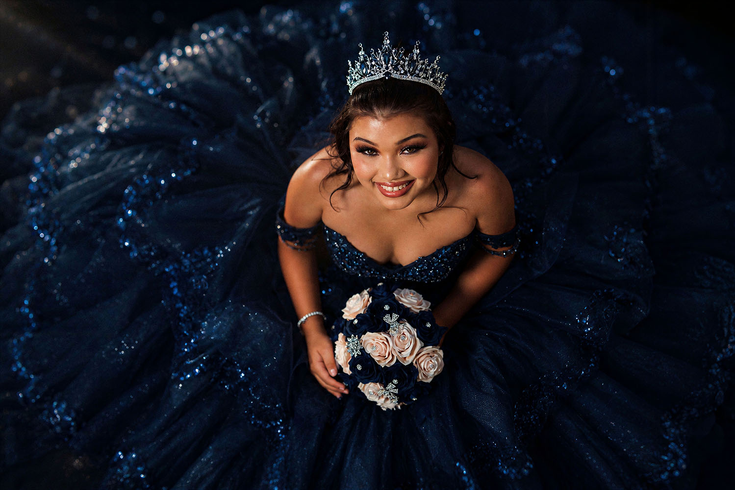 Quinceañera in navy sequined ballgown with crown and bouquet
