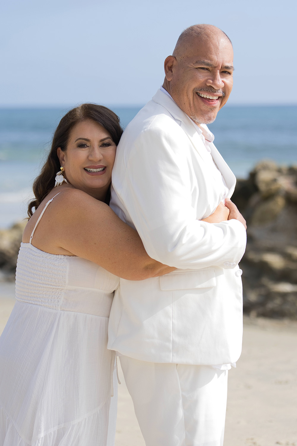 Couple in white embracing on the beach by the ocean